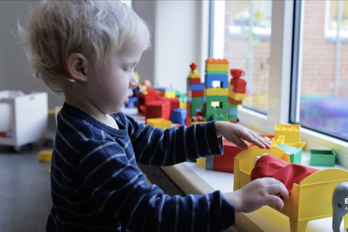 Barn leger med en dukkeseng i en vindueskarm