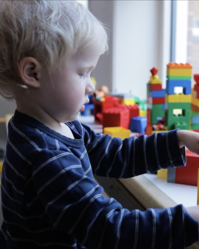 Barn leger med en dukkeseng i en vindueskarm